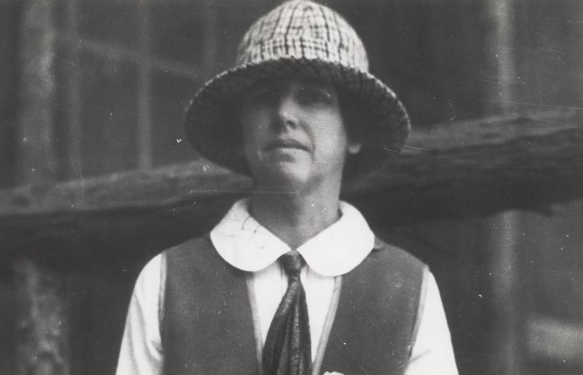 Martha Bingaman poses wearing a skirt, blouse, scarf, soft brimmed hat, and vest. She has a shield-shaped badge pinned to the vest.